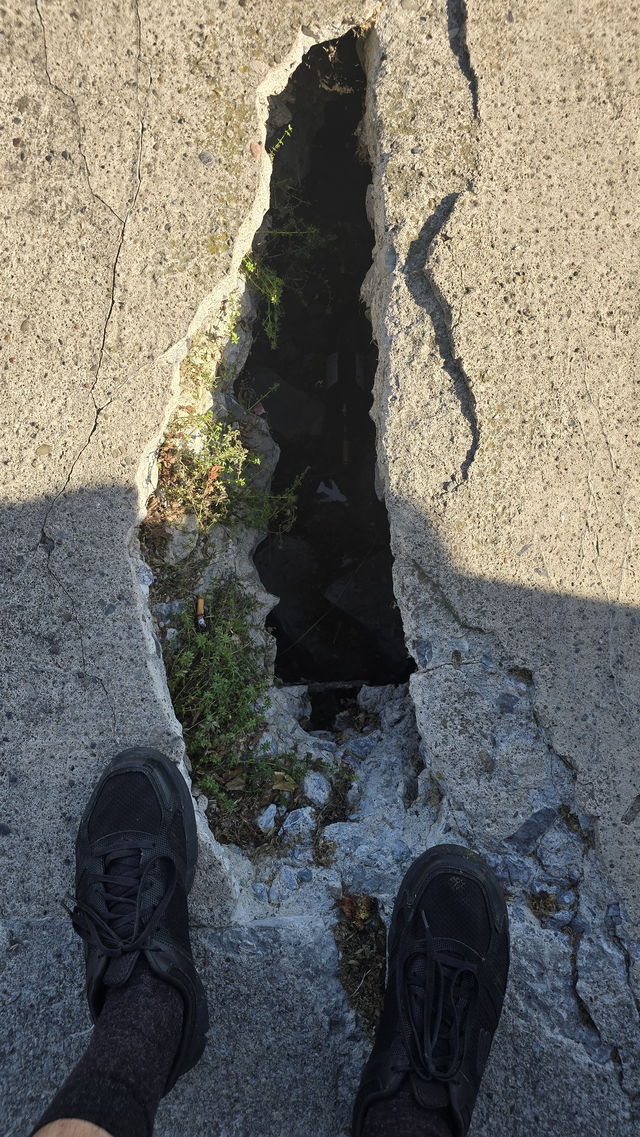 A broken section of the concrete deck exposing a dark void below, next to a walker's feet