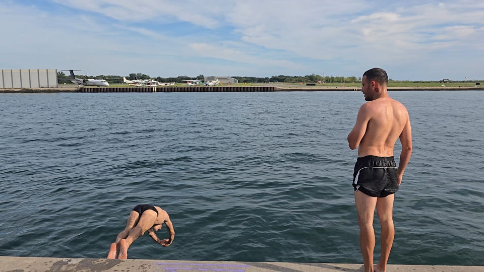 A swimmer arcing into the lake beside the pier's safety ladder