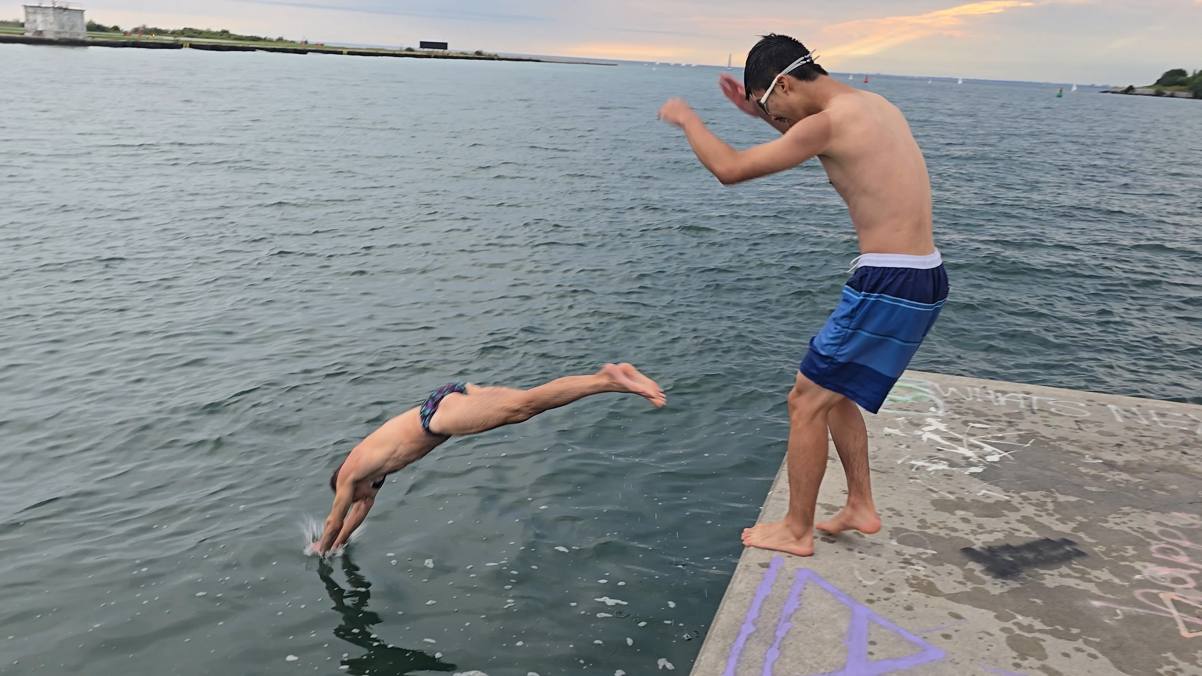Two people jumping off Westmost end of pier