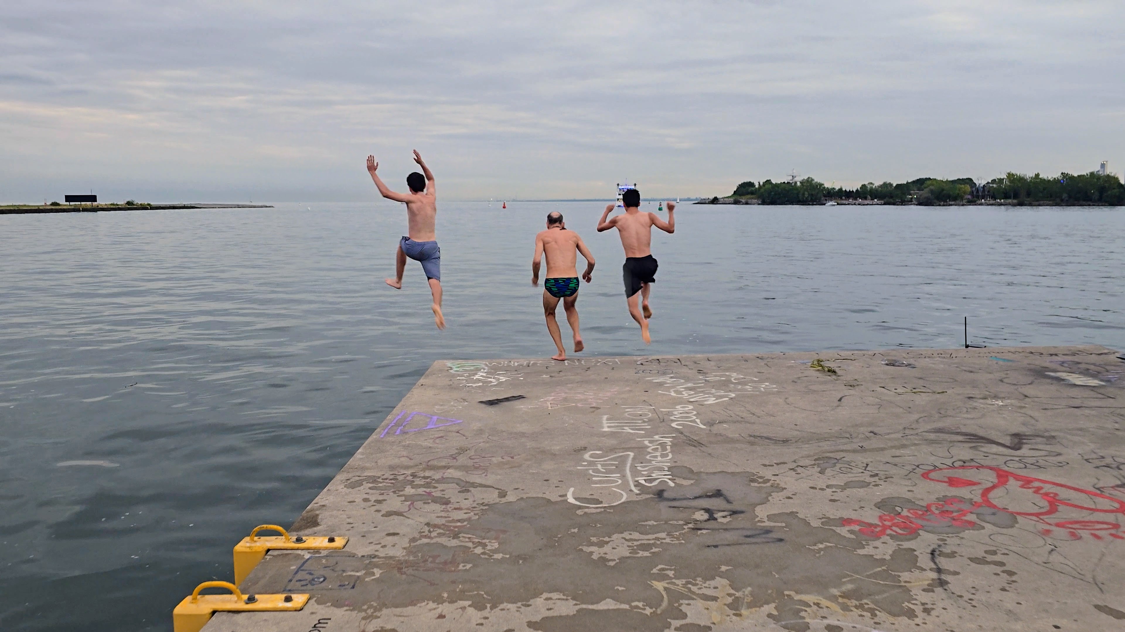 Three people taking a long run off a not so long pier
