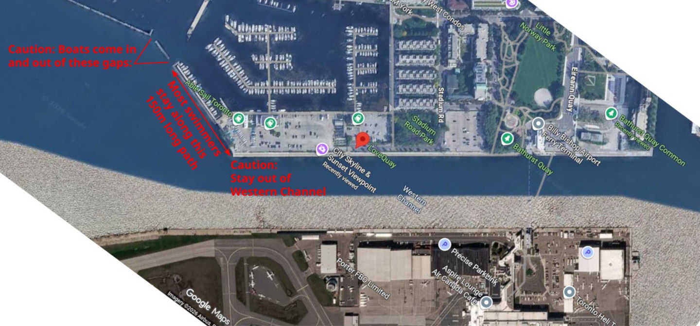 Satellite map of LoveQuay. A red arrow marks the roughly 150-metre stretch along the quay's outer face where most people swim. Labels warn that boats enter and leave through gaps in the marina wall to the north-west, and to stay out of the Western Channel to the south.