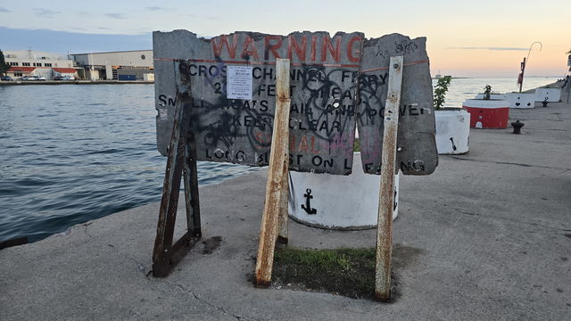 A weathered wooden warning sign about the cross-channel ferry standing at the head of the pier